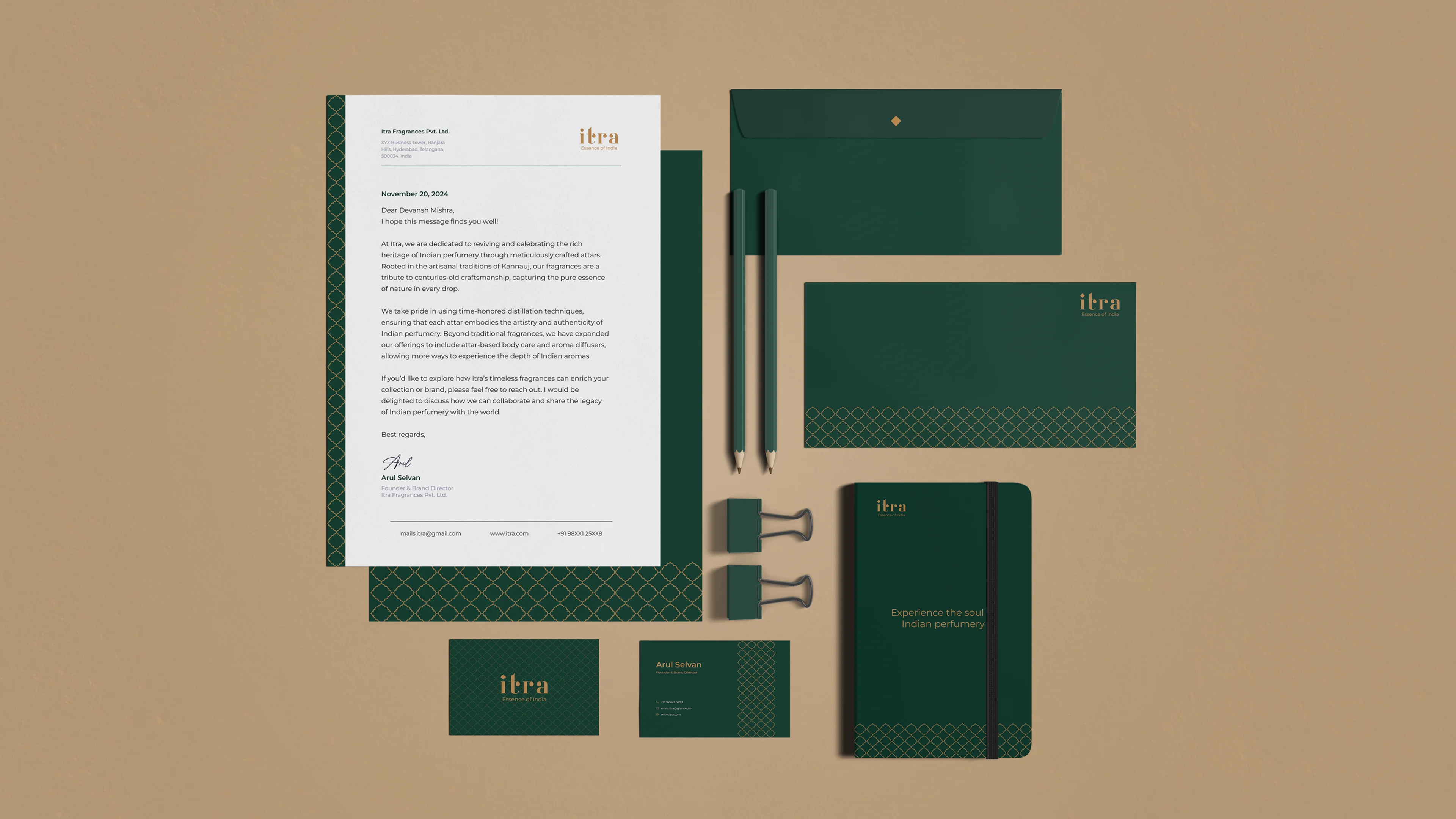 Complete Itra stationery suite on a sand background: letterhead with handwritten signature, dark green envelope, pencils, binder clips, branded notebook, and business cards front and back