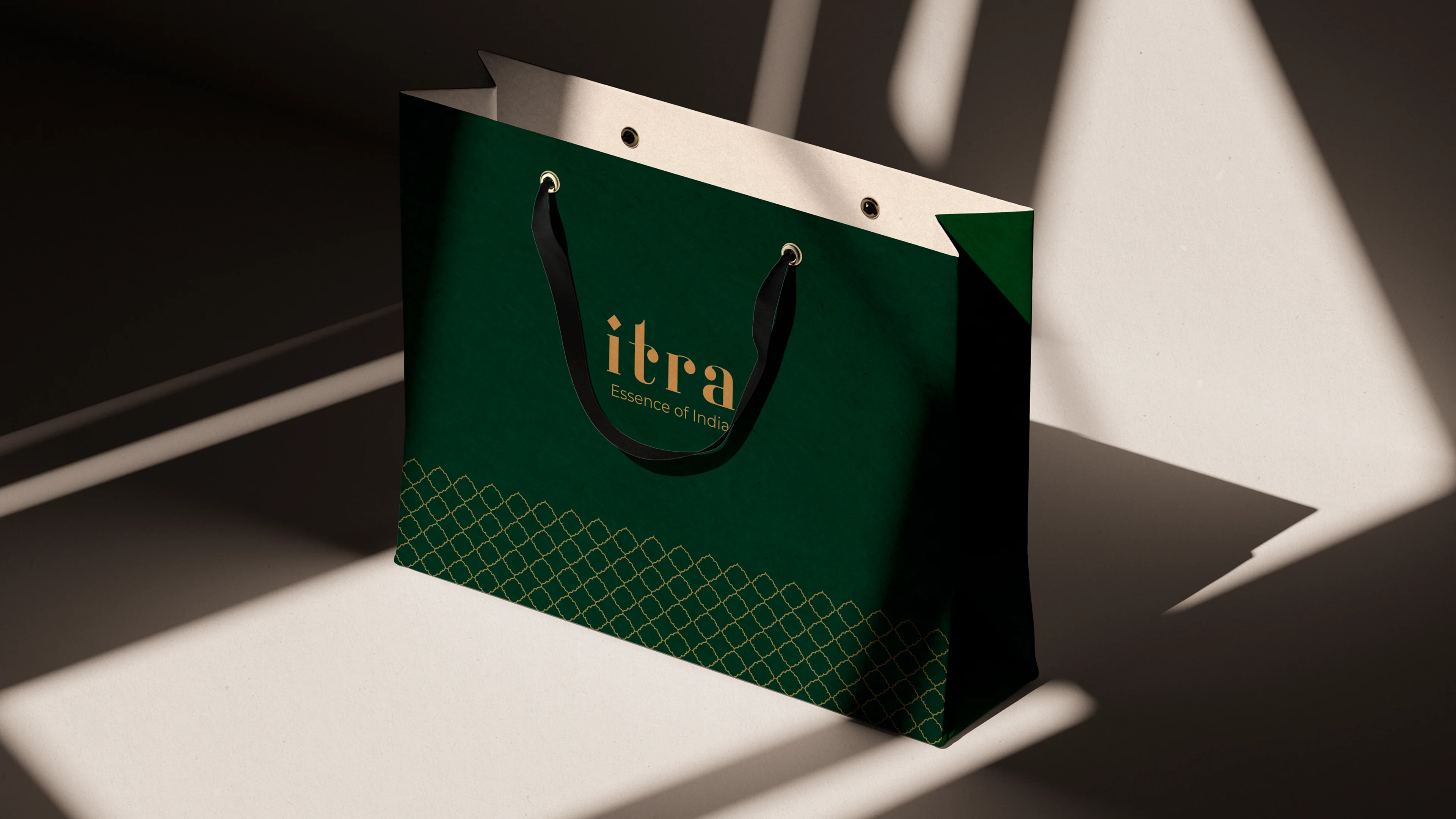 Forest green Itra shopping bag with gold lattice trim border along the base, dramatic directional light casting geometric shadows on a white surface